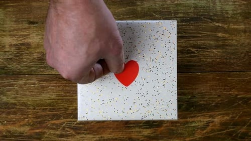 Hands Put Heart on Giftbox on Wooden Table
