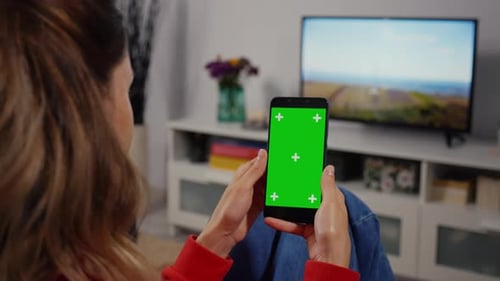 Woman at Home Sitting on a Couch using Smartphone with Green Mock-up Screen