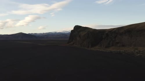 Drone Over Black Sand Terrain Towards Mountains