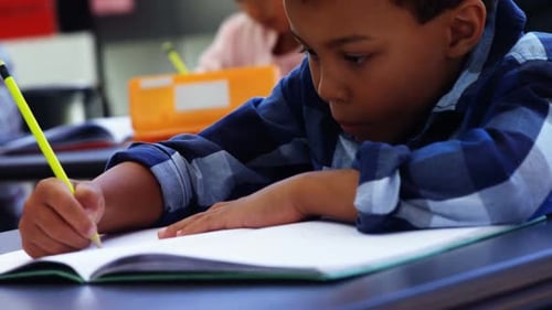 Focused Student Writing in Classroom with Yellow Pencil