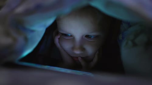 Kleines Mädchen spielt und schaut Smartphone unter Decke