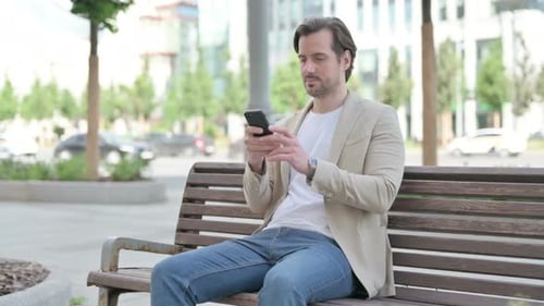 Man Uses Phone Sitting on Park Bench