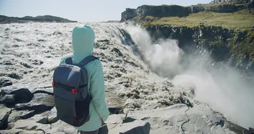 Frau steht am Rand der Klippe und blickt auf den Detifoss-Wasserfall in Island