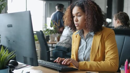 Jolie fille afro-américaine travaillant avec un ordinateur en tapant dans un lieu de coworking