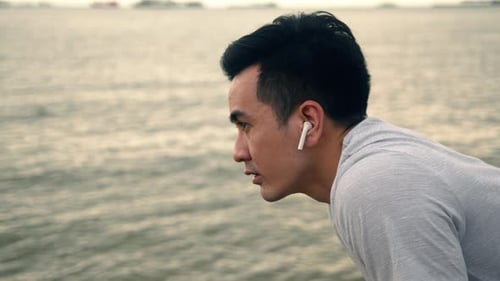Exhausted Asian athlete taking a breath after exercising workout running on the beach.