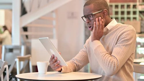 Disappointed African Man Reacting to Loss on Tablet in Cafe