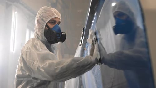 Man Cleans Blue Industrial Equipment Wearing Protective Suit