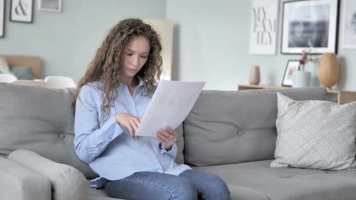 Woman Reviews Documents Sitting on Couch Indoors