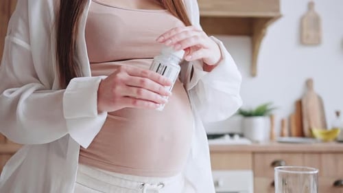 Pregnant Woman Taking Vitamins in Sunny Kitchen