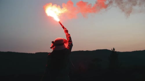 A Young Woman is Standing on the Edge of a Cliff and Waving Flares in the Night