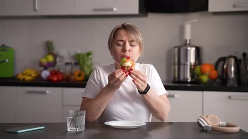 Woman Enjoys a Cupcake in Kitchen at Table