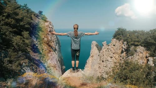 Young Long-haired Inspired Man Raises His Hands Up Standing on the Top of a Mountain Above the Sea