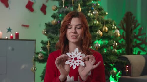 Woman Makes Paper Snowflakes by Christmas Tree
