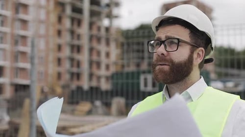 Construction Worker Reviews Blueprints on Building Site