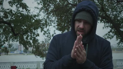 Man in Hoodie Rubs Hands Together Outdoors