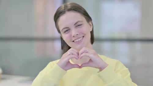 Smiling Young Woman Makes Heart Shape with Hands
