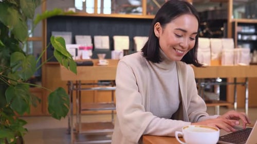 Happy Young Asian Business Woman Having Coffee Break Using Laptop in Cafe