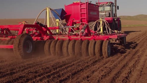 Red seed harvester sows wheat seeds in the field. The machine for sowing seeds works in the field.