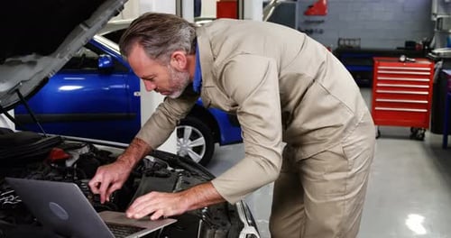 Mechanic using laptop while servicing a car engine