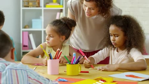 Children Drawing with Teacher Assistance in Bright Classroom