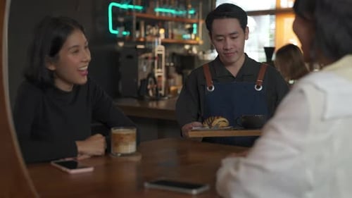 Garçom de homem asiático 4K servindo café com leite e padaria para cliente mulher na mesa do café