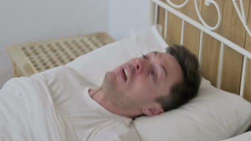 Un jeune homme effrayé se réveille d'un cauchemar au lit