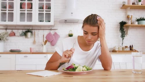 Frau sitzt am Tisch und fühlt sich unzufrieden mit der Diät, die keinen Salat essen will
