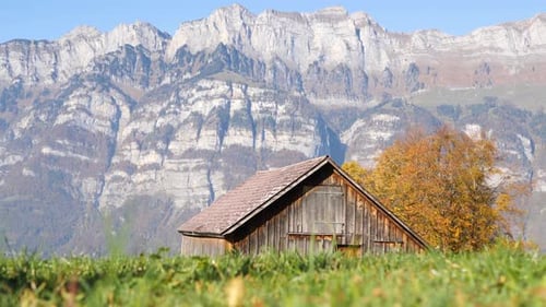 Magnifique paysage avec une cabane et de grandes montagnes en arrière-plan. La caméra s'élève du sol.