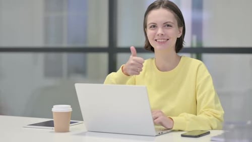 Young Woman Showing Thumbs Up Sign While Using Laptop in Office
