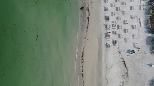 Slow motion video of waves crashing on the beach in front of a beach resort. Beach chairs line the b
