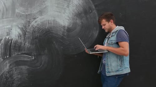 Man Uses Laptop in Front of Urban Mural