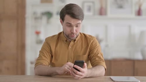 Man Celebrating Good News on Smartphone Indoors