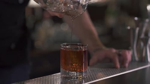 Bartender Pouring Dark Liquor Into Glass with Ice