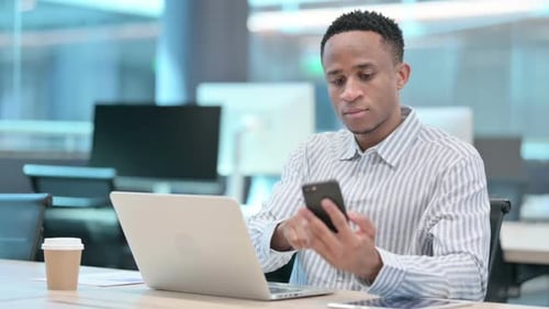 Young Adult Uses Laptop and Mobile Phone in Office
