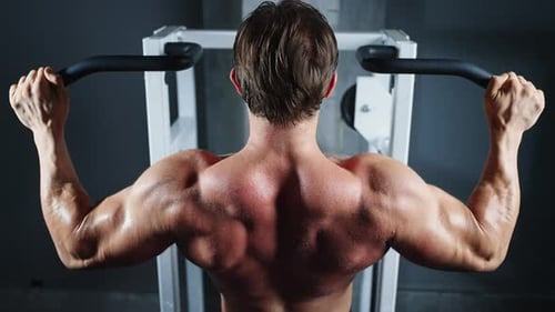 4K Caucasian man bodybuilder pulling up body weight lifting at gym.