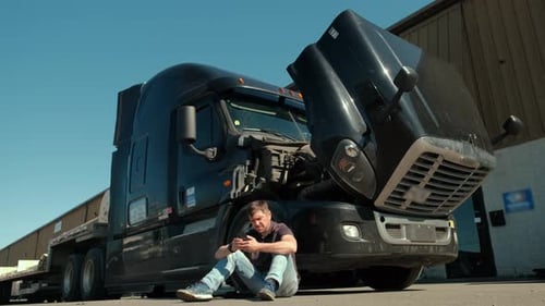 Man Sits near Truck with Open Hood