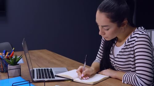 Focused Woman Writing at Desk in Modern Office