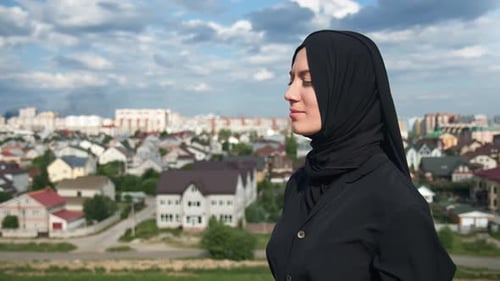 Agréable femme musulmane en foulard noir traditionnel debout sur le sommet de la montagne au-dessus de la ville islamique