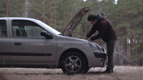 Young Man Inspecting Car Engine in Rural Setting