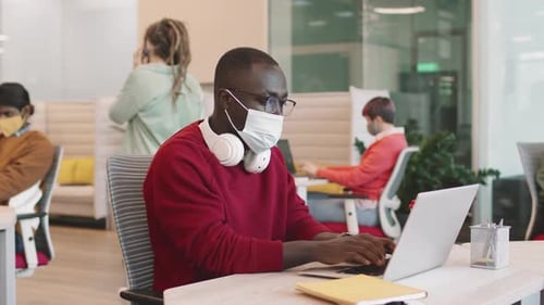 Homme d'affaires noir portant un masque facial travaillant au bureau