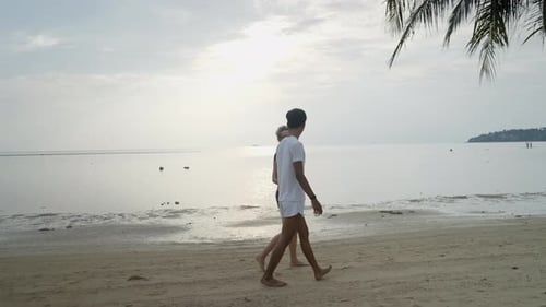 Interracial Couple Walking Holding Hands Along the Sea at a Tropical Island Beach on Sunset