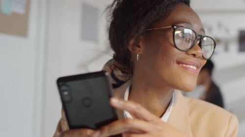Afro-American Female Office Worker Smiling and Messaging on Smartphone