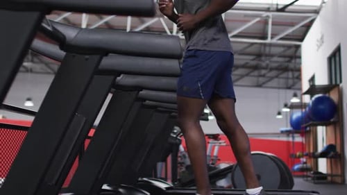Fit african american man with face mask around his neck running on treadmill in the gym