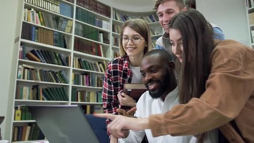 Modern Multiethnic Friends Working Over Home Task in the Library Using Computer