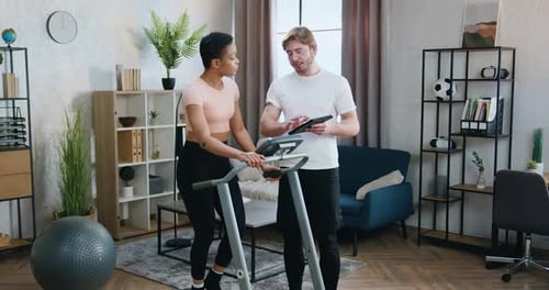 Pareja entrenando juntos en una cinta de correr usando instrucciones especiales de acondicionamiento físico en una tableta en casa