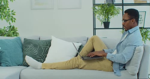 Man Relaxes on Couch While Using Laptop