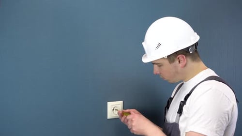 An Electrician Repairs an Outlet in the House