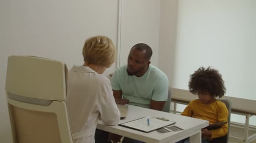 Professional Woman Doctor Explaining Medical Treatment to Worried Black Dad During Visit at Hospital