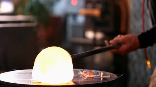 Glassblower rolling molten glass on pieces of colored glass