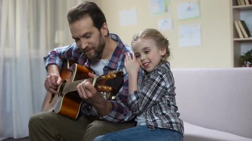 Father Plays Guitar for Child on Couch